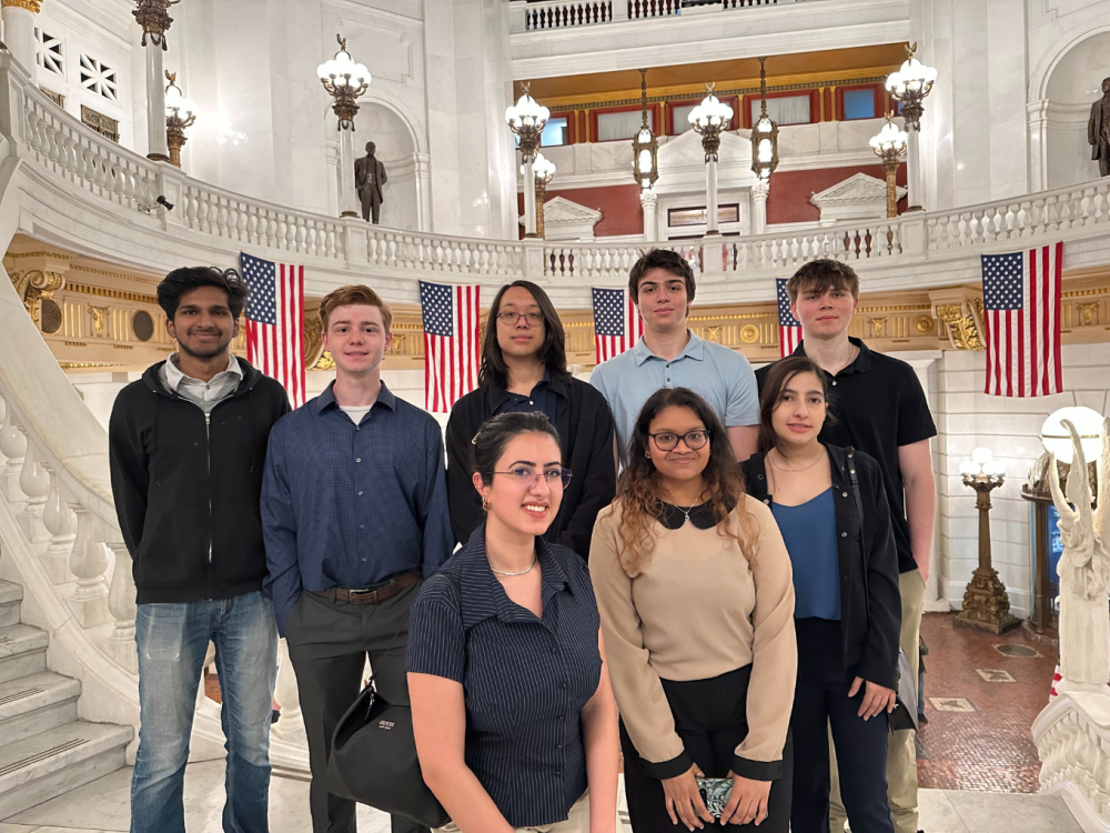 Eight people smile on the steps inside the Capitol Building in Harrisburg